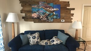 A living room with a blue sofa, two lamps, and a wall art piece depicting a sea turtle.