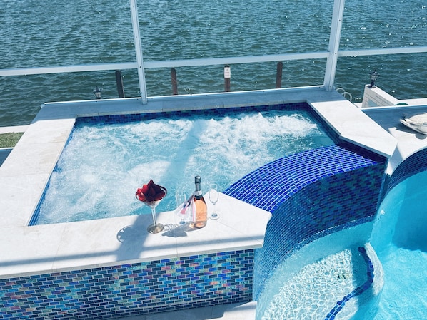 A hot tub with a view of the water, a bottle, and a glass.