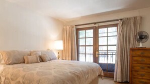 Un dormitorio con una cama grande, un aparador, un ventilador y una ventana con cortinas.