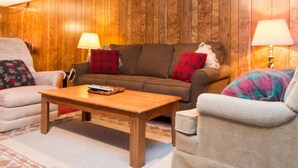 Una sala de estar acogedora con una pared de madera, un sofá marrón con cojines rojos y negros, un sillón beige y una mesa de centro de madera.