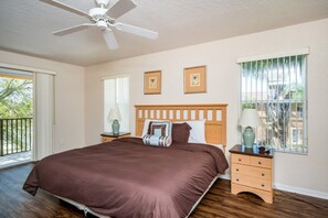 Ein Schlafzimmer mit einem großen Bett, einem Deckenventilator, einem Nachttisch mit Lampe und einem Fenster mit Jalousien.