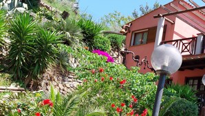 Un edificio con fachada roja, rodeado de exuberante follaje y flores vibrantes.