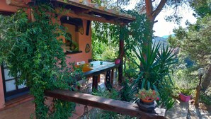 Un espacio al aire libre rústico con una mesa y sillas de madera, rodeado de follaje exuberante y plantas en macetas.