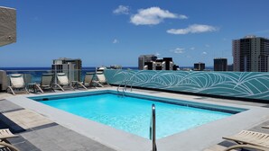 A rooftop pool with lounge chairs and a city view.