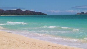 A beach with clear turquoise waters, a sandy shore, and distant mountains.