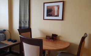 Un coin repas avec une table ronde en bois, deux chaises, un tableau encadré au mur et un rideau à motifs.
