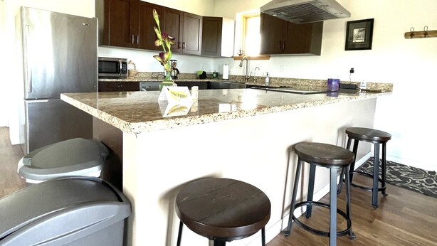 A modern kitchen with a central island, bar stools, a refrigerator, microwave, and a clock on the wall. - Beautiful Apartment With Great Views In The Colorado Countryside. (Durango)