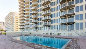 Une piscine dotée d’une terrasse carrelée, entourée d’un immeuble à plusieurs étages avec des balcons.