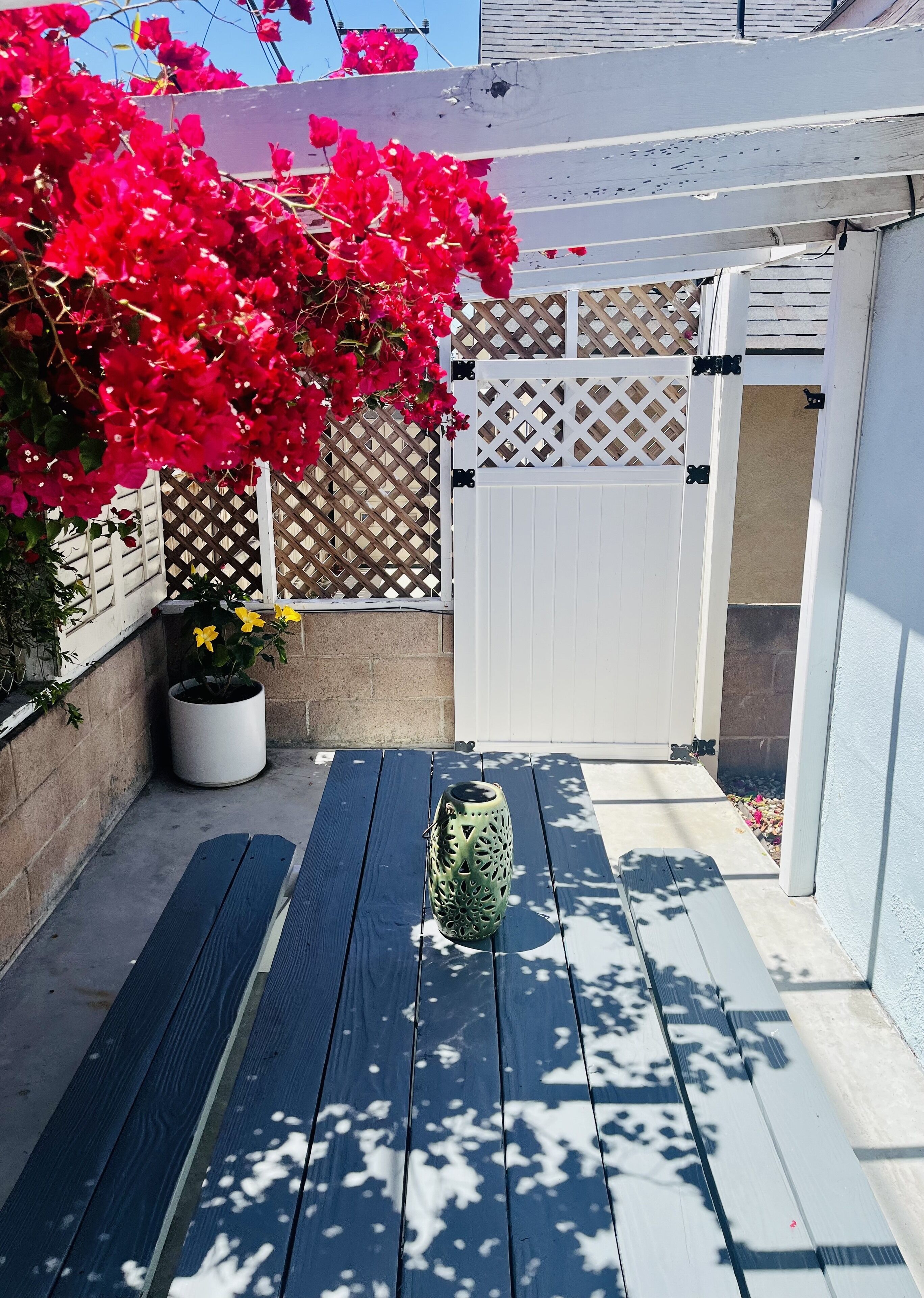 A patio with a wooden deck, a white gate, and a potted plant.