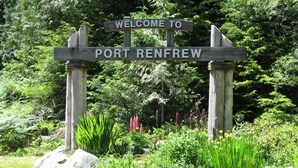 Un panneau indicateur en bois sur lequel on peut lire « BIENVENUE À PORT RENFREW », entouré de rochers et de verdure.