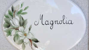 En hvid keramisk tallerken med ordet "Magnolia" og et blomstermotiv.