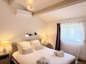 Quarto de hotel com cama, duas luminárias de cabeceira, ar-condicionado fixado na parede e janela com cortinas.