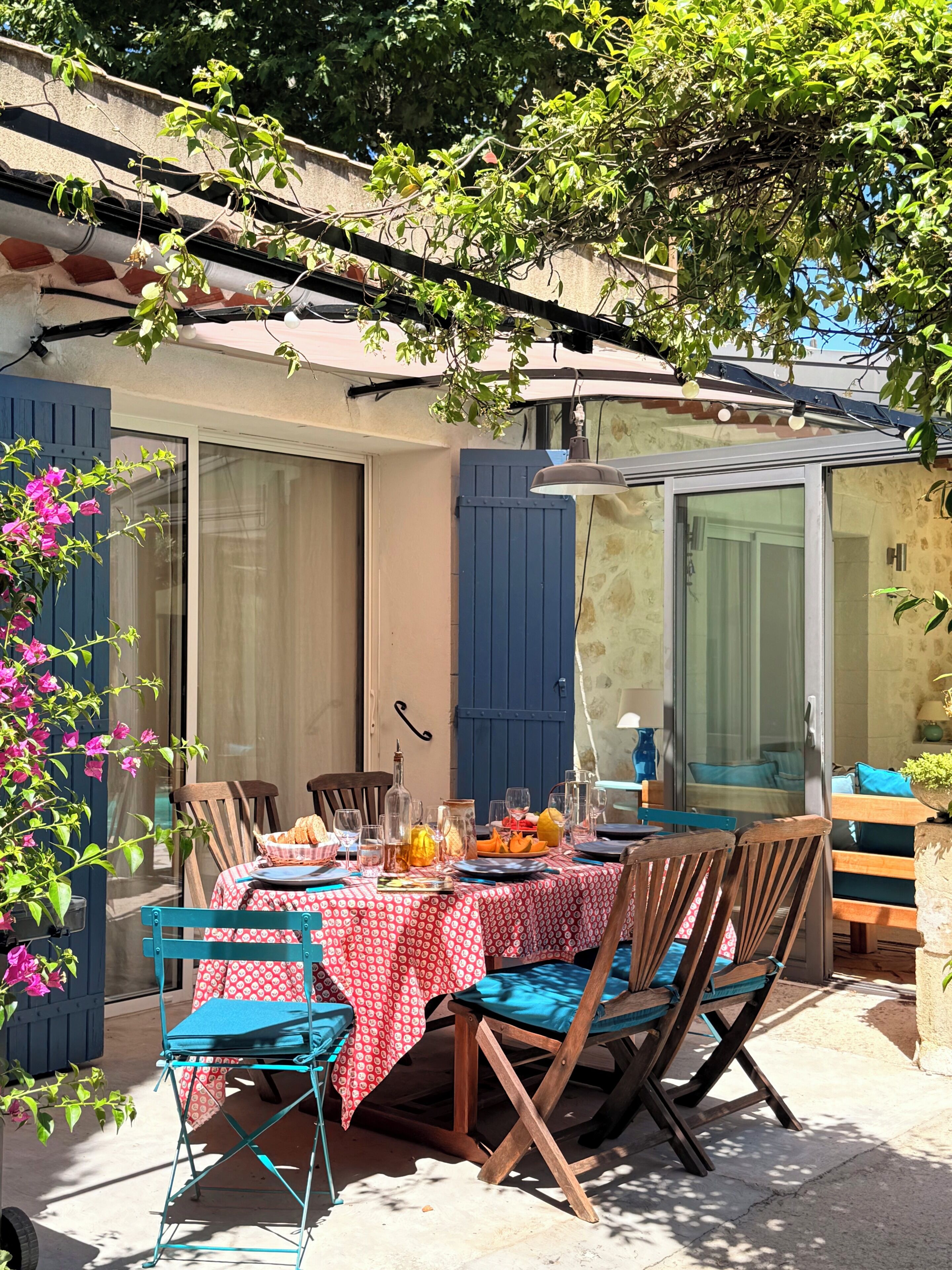 Een terras met een tafel gedekt voor twee personen, omringd door houten stoelen met blauwe kussens.