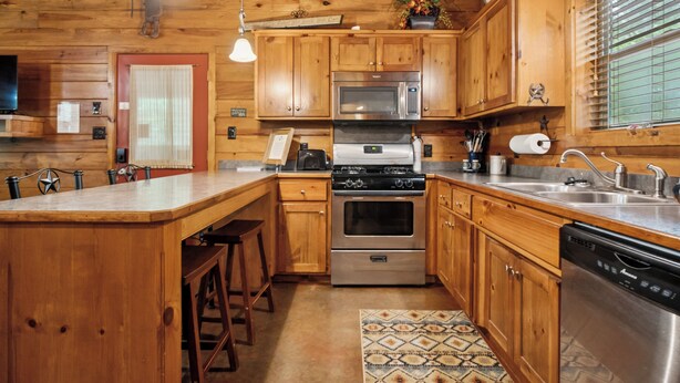 Una cocina tipo cabaña de madera con una isla central, electrodomésticos de acero inoxidable y lámparas colgantes.
