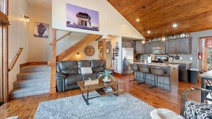 A spacious living area with a wooden ceiling, a staircase, a kitchen with modern appliances, and a dining area.