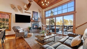 A spacious living room with a fireplace, leather sofa, and a large window offering a view of the outdoors.