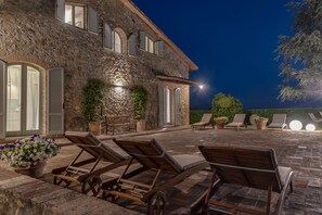 A stone building with a patio area featuring lounge chairs and potted plants.