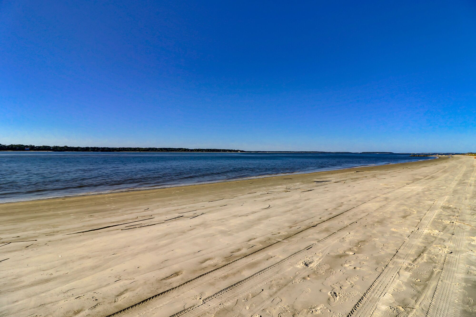 Ein weiter, sandiger Strand mit blauem, wolkenlosem Himmel.