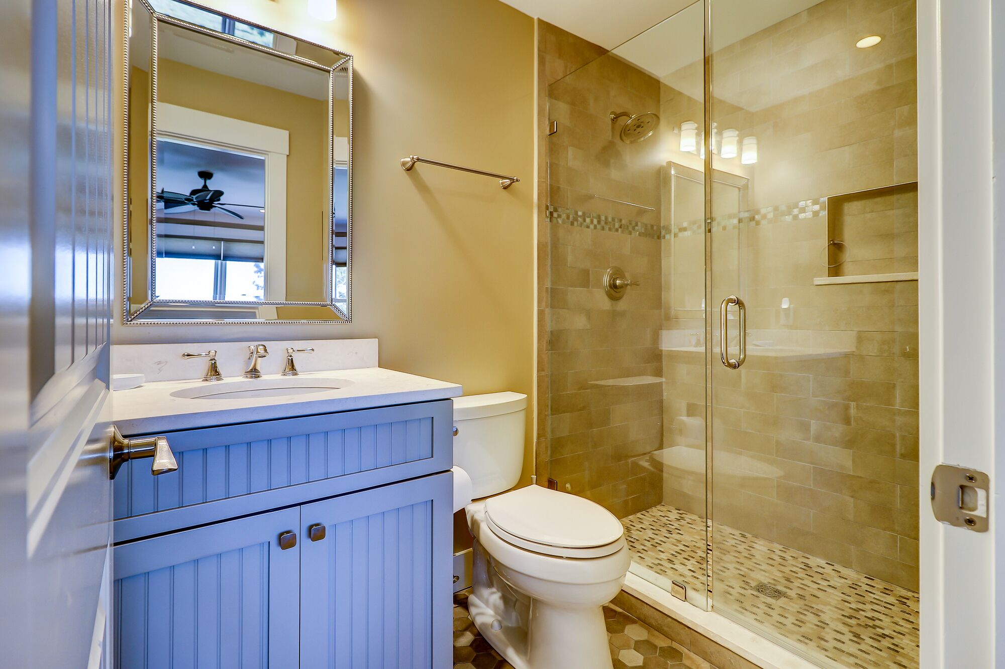 A bathroom with a glass-enclosed shower, a white toilet, and a vanity with a mirror and sink.
