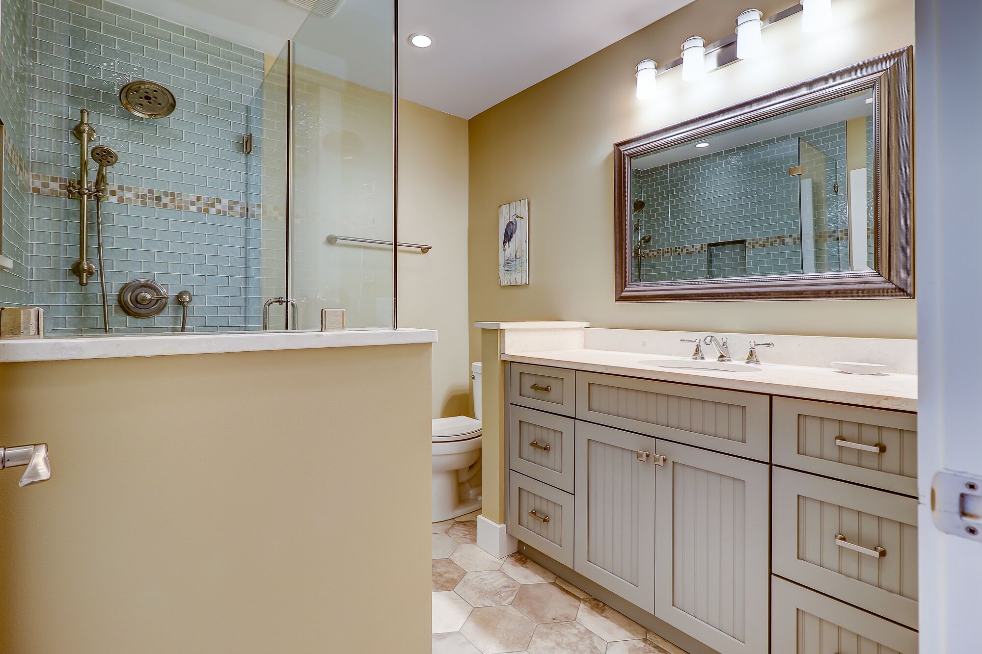 Un baño con cabina de ducha de vidrio, un espejo grande y un mueble de tocador con varios cajones.