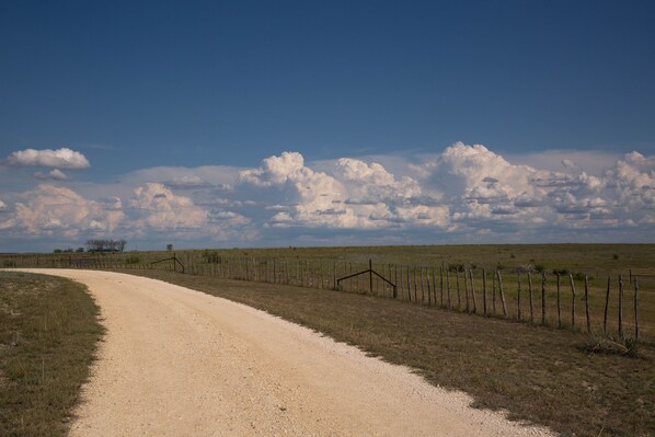 Un camino rural de tierra con una cerca a un lado y un cielo despejado con nubes.