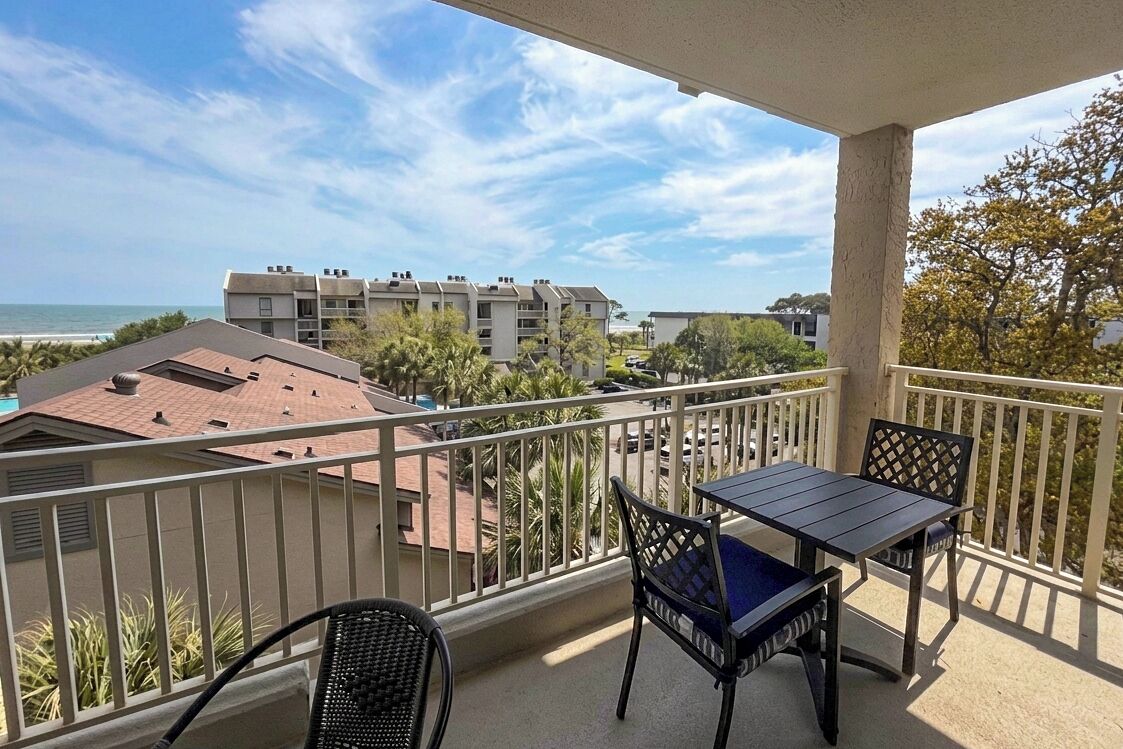 A balcony with a table and chairs, overlooking a beach and other buildings.