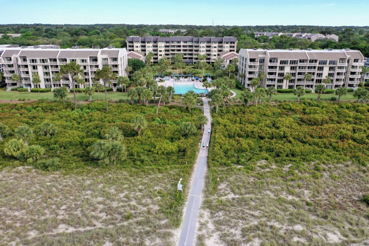 A resort with multiple buildings, a central pool area, and a pathway leading to the pool surrounded by greenery.