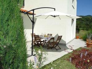 An outdoor patio with a table and chairs, a white umbrella, and potted plants.