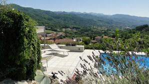 Ein Poolbereich mit Liegestühlen und Blick auf ein Dorf und Berge.