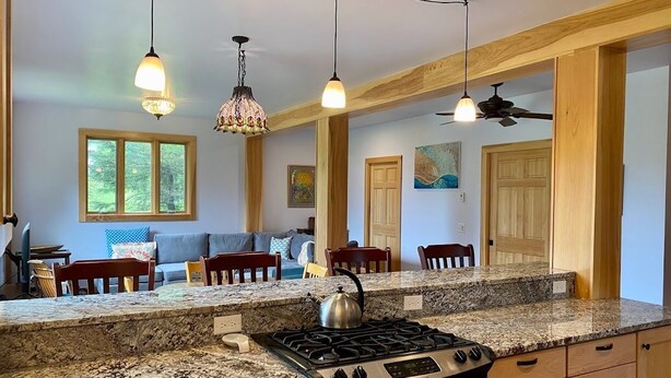 Une cuisine dotée de plans de travail en granit, d’une cuisinière à gaz, d’armoires en bois et de luminaires suspendus.