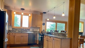 Une cuisine dotée de meubles en bois, de plans de travail en granit, d’une cuisinière et de luminaires suspendus.