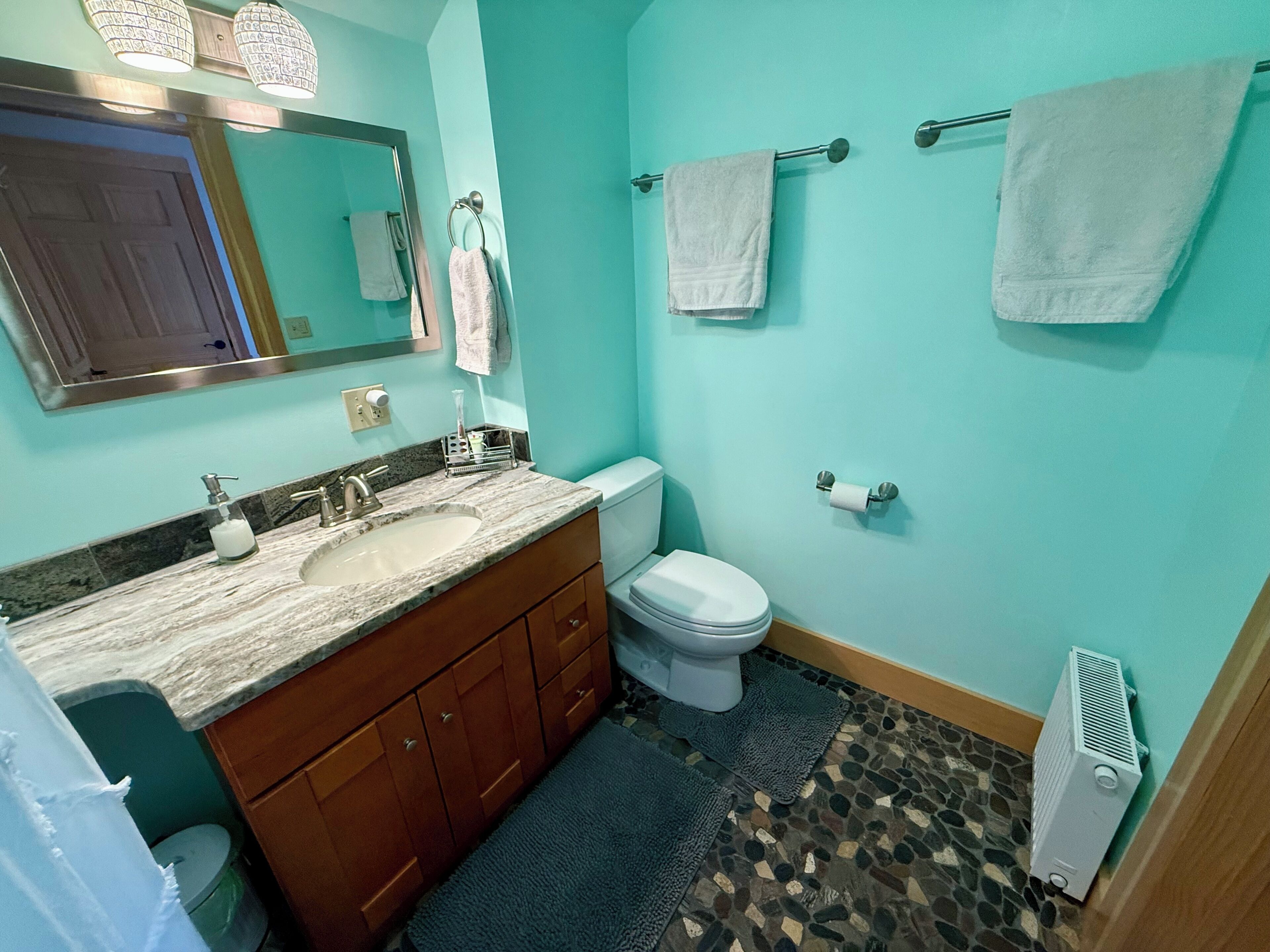 Een badkamer met een wastafel, toilet en spiegel. Handdoeken hangen aan een rek.
