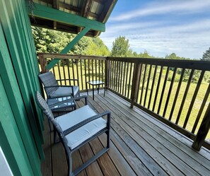 Une terrasse en bois avec deux fauteuils en osier et une petite table, donnant sur une zone herbeuse.