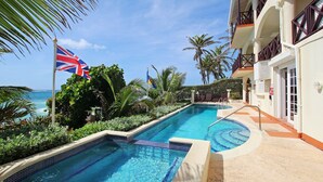 Piscina con vista al océano, rodeada de palmeras y un edificio con balcones.