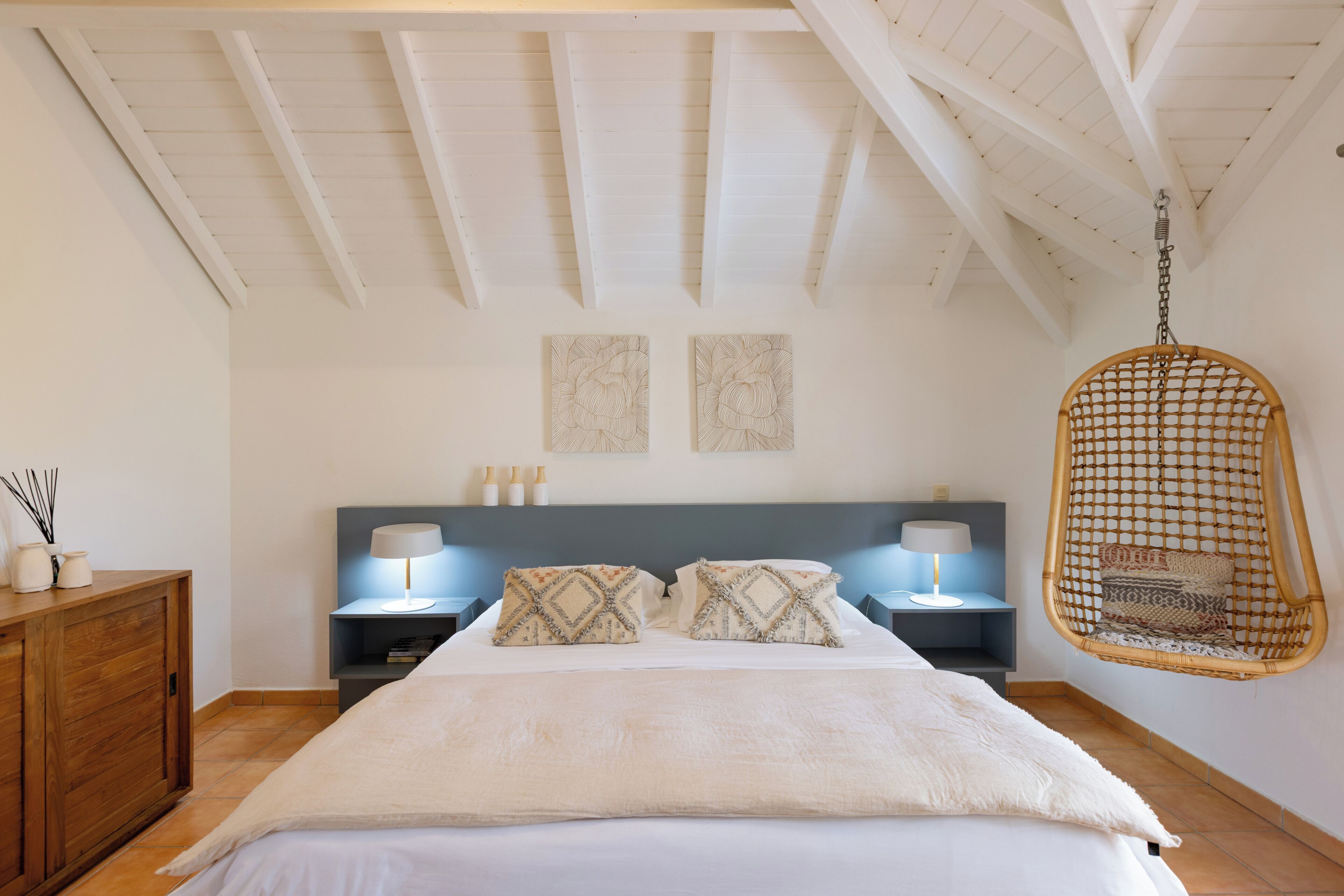 A bedroom with a bed, two wall-mounted lamps, a hanging chair, and a wooden cabinet.
