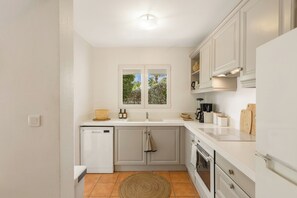 A compact kitchen with white cabinets, a built-in dishwasher, a window above the sink, and a small rug on the floor.