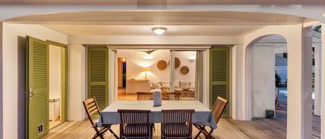 A covered outdoor dining area with a table and chairs, a lamp, and a view of the interior.