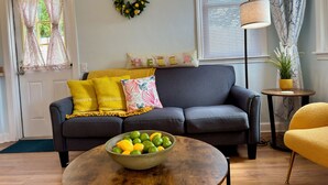 A living room with a sofa, a coffee table with a bowl of fruit, a lamp, and a potted plant.