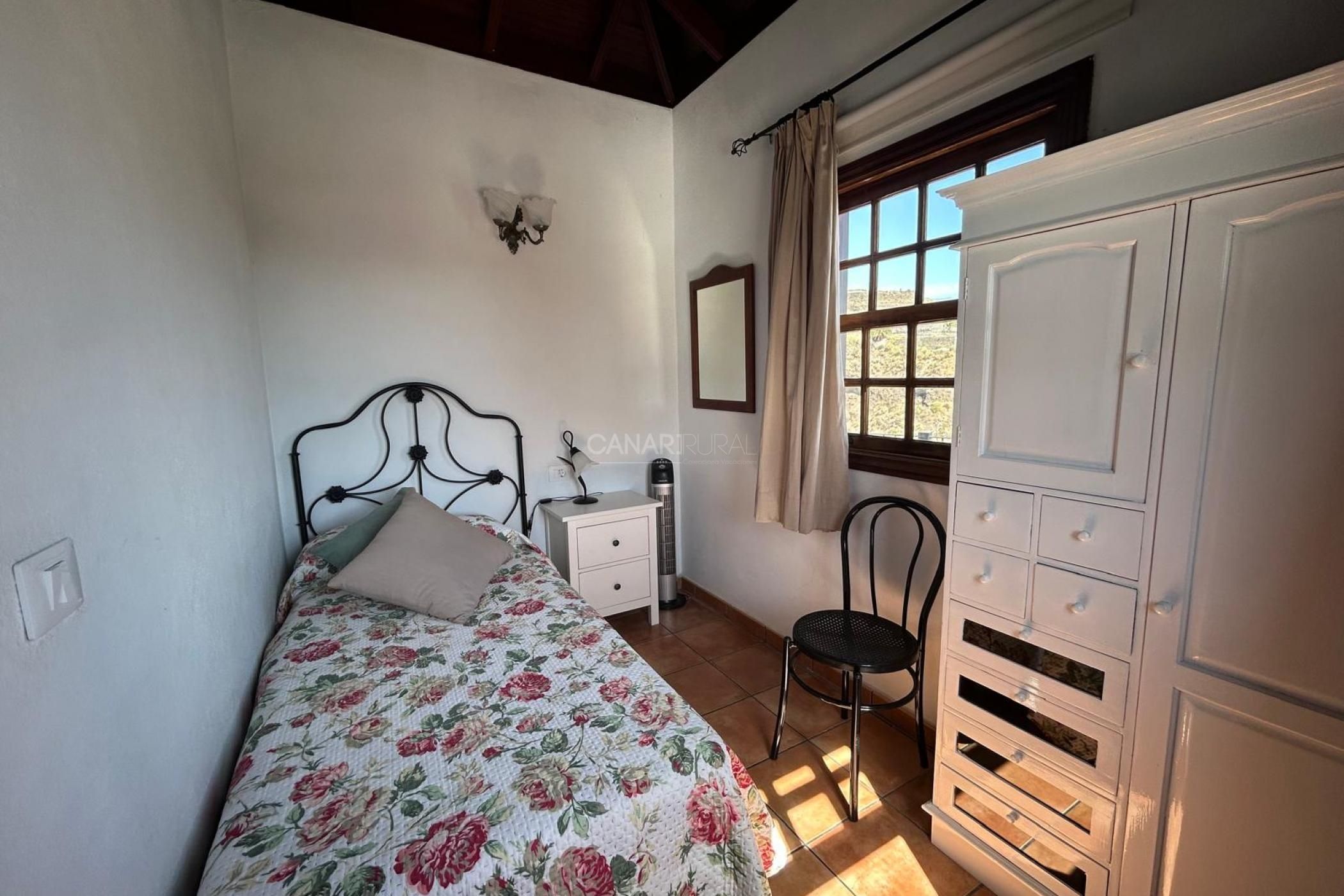 Une chambre à coucher comprenant un lit, une table de chevet, une chaise, une armoire et une fenêtre avec des rideaux.