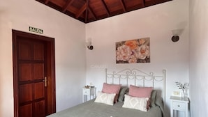 Un dormitorio con una cama, una puerta de madera con la leyenda 'SALIDA', un cuadro colgado en la pared y una mesita de noche blanca.