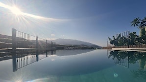 Piscina cristalina con vistas a la montaña, rodeada por una cerca y palmeras.