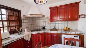 Una cocina con armarios rojos, salpicadero de azulejos, una ventana con persianas y una lámpara colgante.