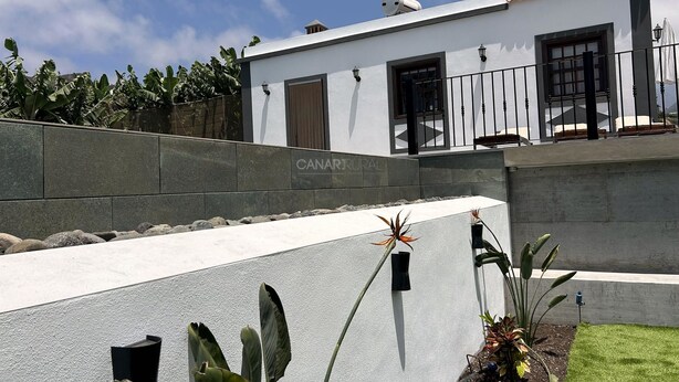 A modern building with a white facade, a stone retaining wall, and a small garden area with plants.