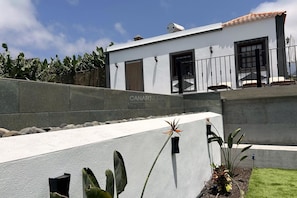 Un edificio moderno con fachada blanca, un muro de contención de piedra y un pequeño jardín con plantas.