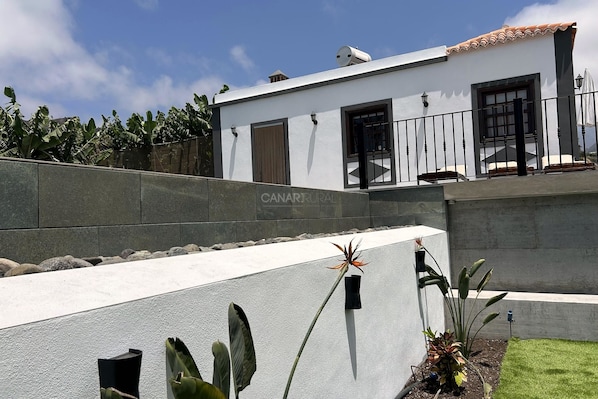 Un edificio moderno con fachada blanca, un muro de contención de piedra y un pequeño jardín con plantas.