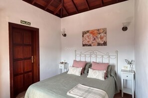 A bedroom with a bed, a wooden door labeled 'SALIDA,' a wall-mounted painting, and a white nightstand.