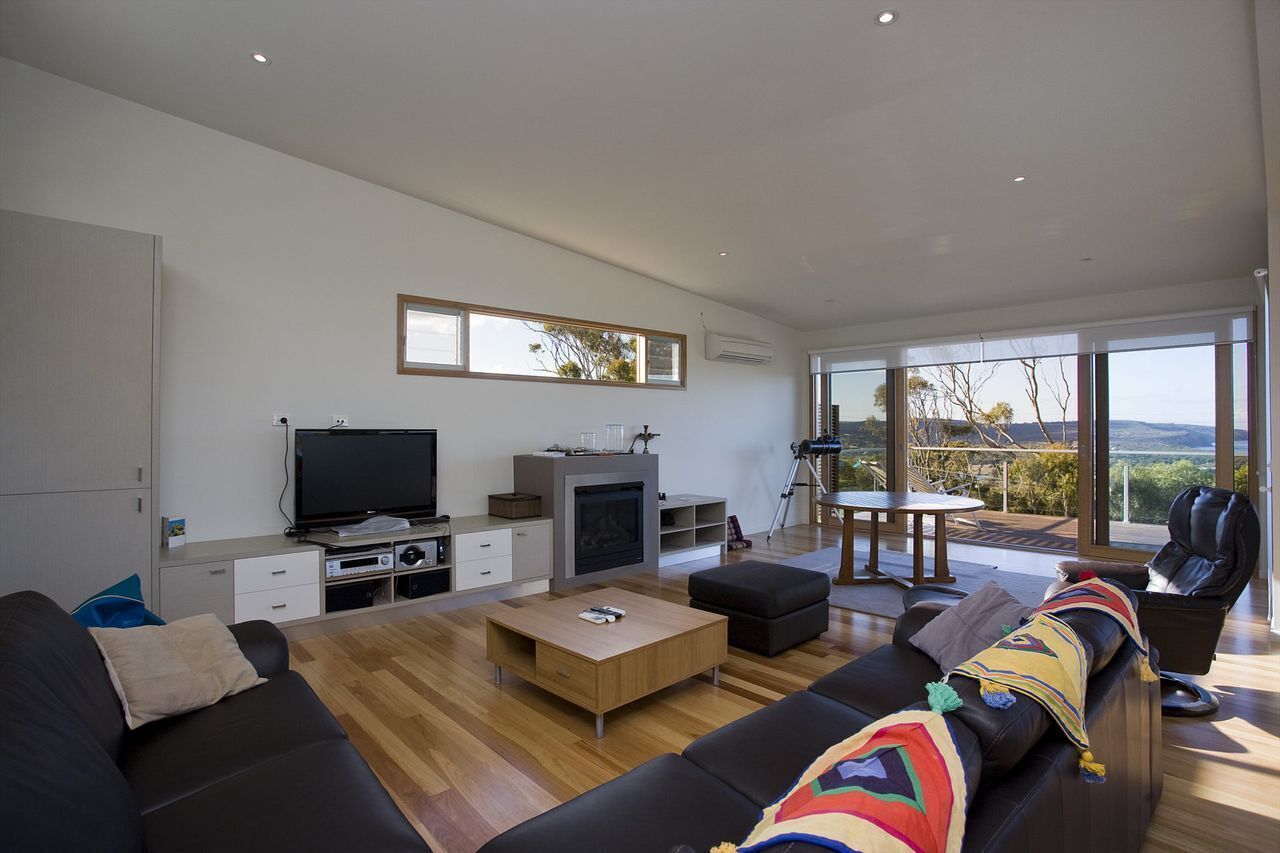 A modern living room with a flat-screen TV, fireplace, and large windows offering a view of the outdoors.