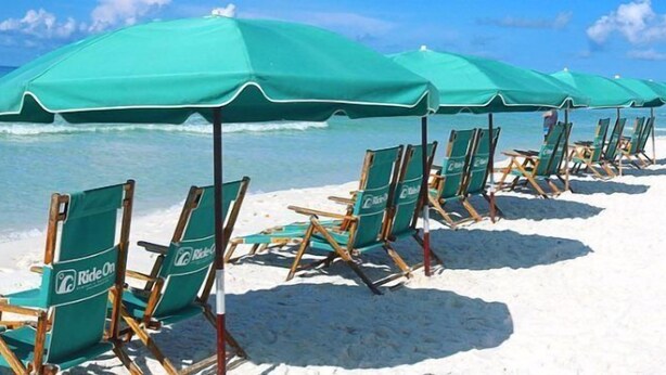A beach with rows of green chairs and umbrellas, some of which are occupied. - Relaxation #201 Free Beach Service Included Chateau La Mer II 1st Fl (Destin)