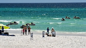 A beach with jet skis, a parasail sign, and people on the sand.