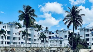 Een hotel aan het strand met meerdere witte gebouwen, balkons en palmbomen.